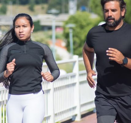 Active couple jogging outdoors on a sunny day, promoting fitness and healthy lifestyle.