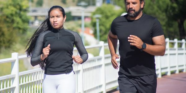 Active couple jogging outdoors on a sunny day, promoting fitness and healthy lifestyle.